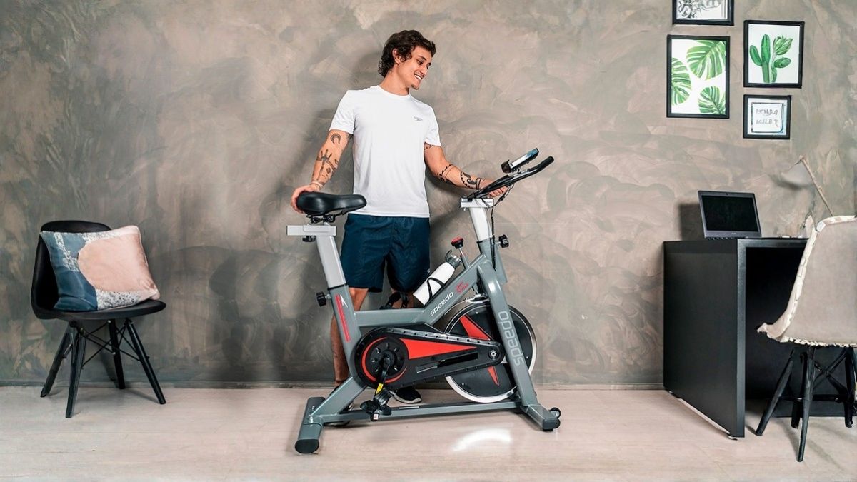Bicicleta spinning Speedo S103 cinza com painel LCD e conexão Bluetooth em ambiente residencial
