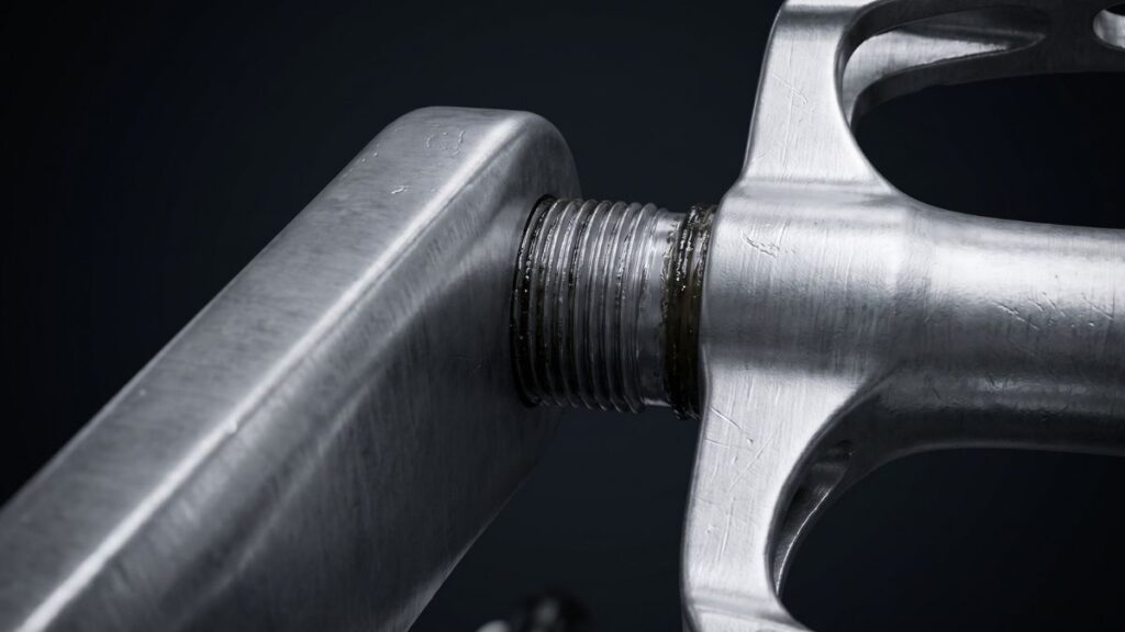 Close fotorrealista de um pedal de alumínio encaixado no braço do pedivela, ressaltando as roscas e a área de suporte de peso.
