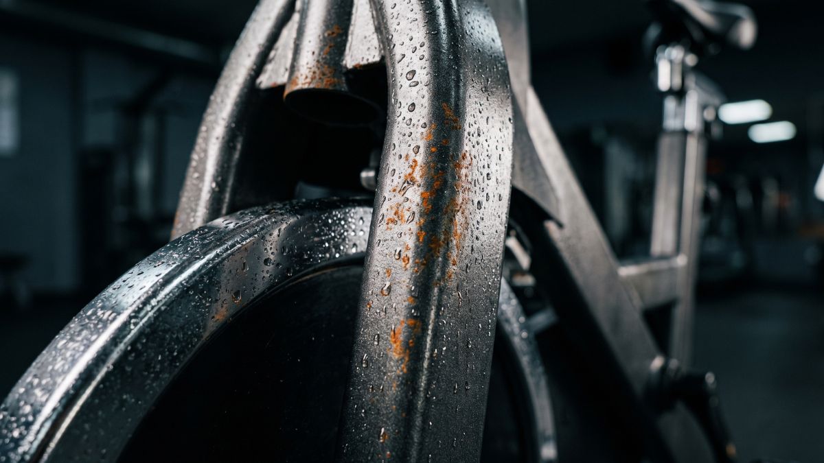 Detalhe de gotas de suor sobre a estrutura de metal de uma bicicleta ergométrica, ilustrando o perigo da corrosão nas peças.