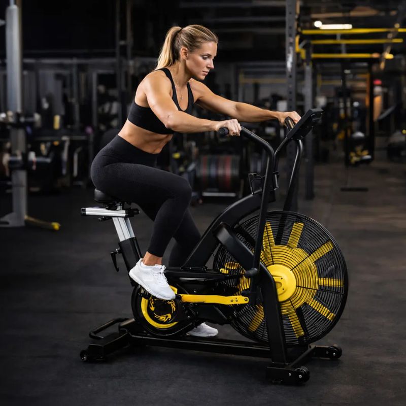 Mulher usando a Bicicleta Ergométrica Air Bike DOAF Profissional em um treino na academia