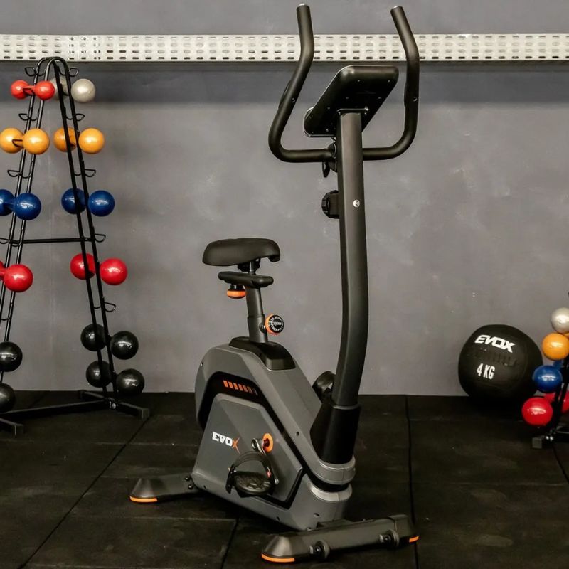 Bicicleta Ergométrica Vertical Evox Fitness V8620 em ângulo frontal exibindo painel e estrutura grafite e preta
