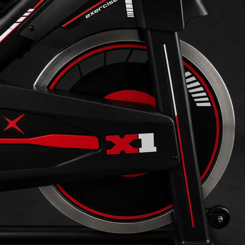 Bicicleta Spinning Evox X1 preta e vermelha vista lateral completa.