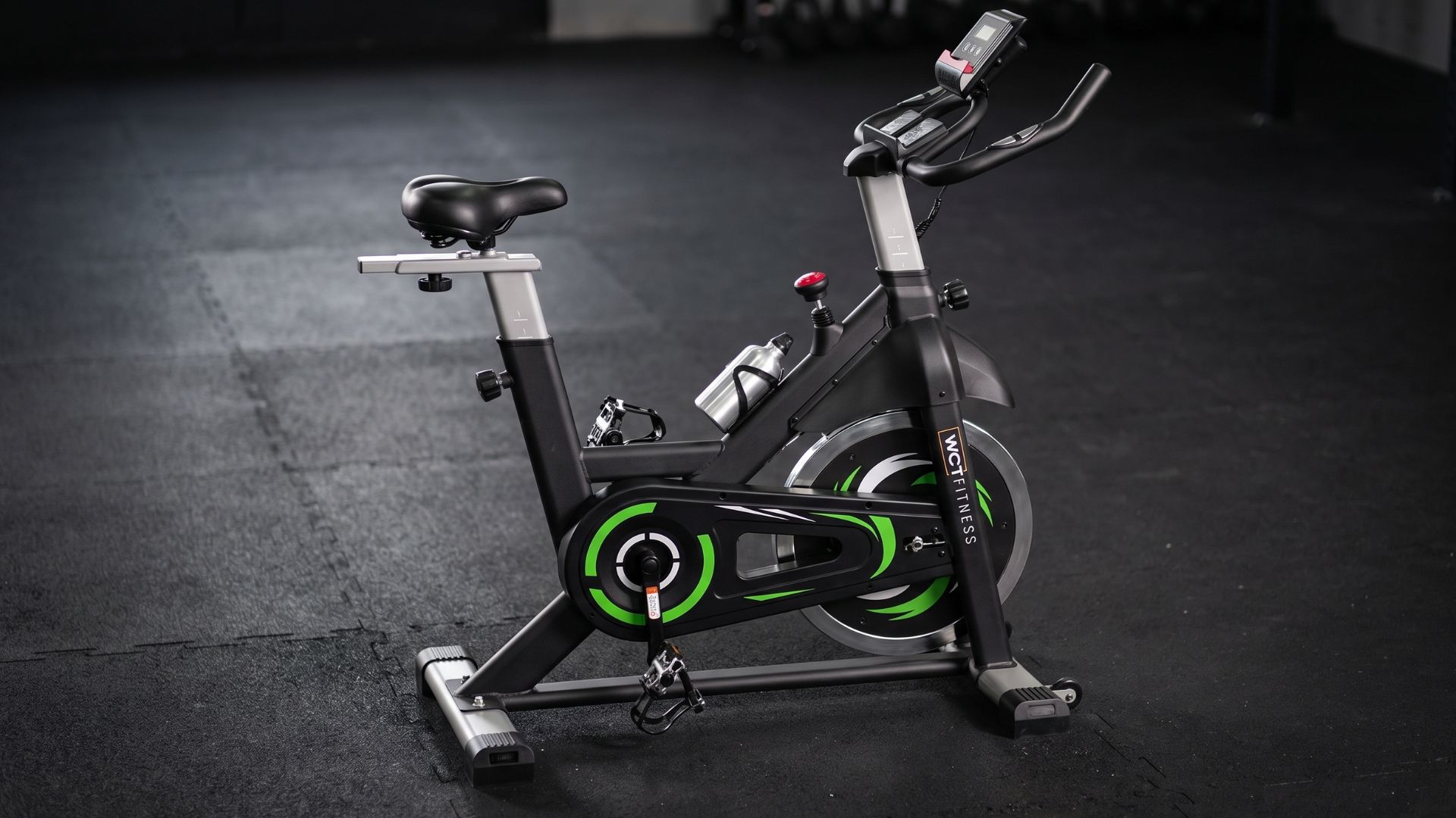 Bicicleta Spinning WCT Fitness 20kg preta e verde em ambiente de treino residencial